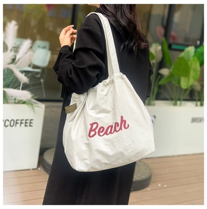 Detalle del bolso tote de lona blanca con texto Beach rojo y diseño de cordón