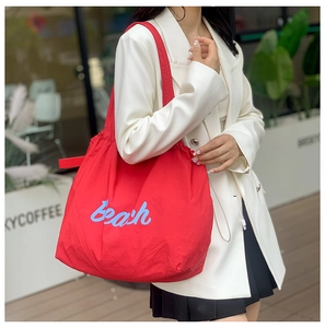 Detalle del bolso tote de nailon rojo con bordado azul y cierre de cordón ajustable