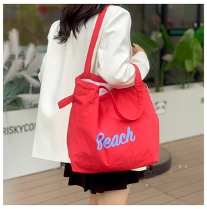 Detalle del bolso tote de lona roja con bordado Beach sobre una chaqueta blanca