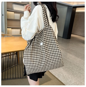 Checkered canvas tote bag shown on shoulder in a cozy indoor lifestyle setting