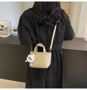 Minimalist beige mini tote bag with monster charm shown in a crossbody style