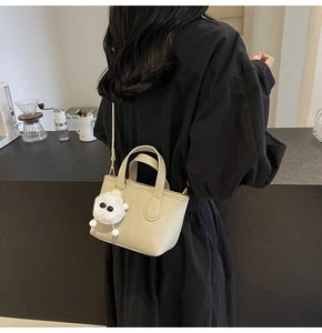 Detail of beige lychee textured bucket bag with cute plush pendant and slim shoulder strap