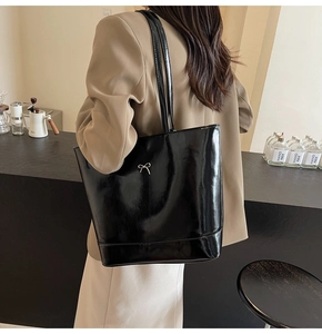Detail of black patent leather tote bag with silver bow accent on model in cafe