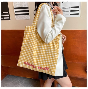 Detail of yellow checkered canvas tote bag featuring sleep well red print and shoulder strap