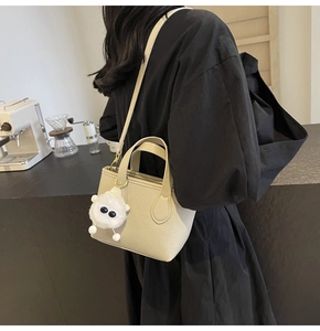 Detail of beige bucket bag with lychee leather texture and cute plush monster charm