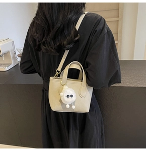 Close-up of beige pebbled leather bucket bag with a cute white plush monster charm