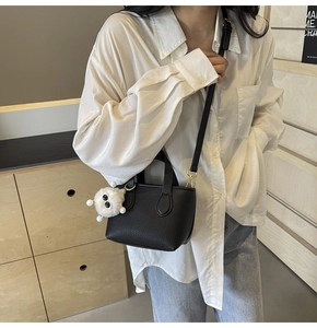 Close-up of black lychee grain leather mini bucket bag with a cute white plush monster charm