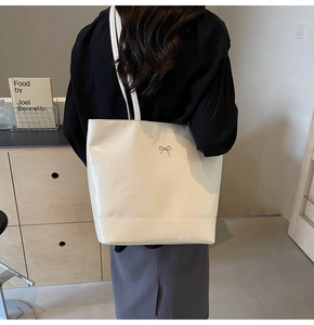 Detail of off-white glossy tote bag with silver bow buckle and shoulder strap worn by model