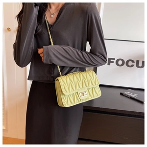Close-up of a light green quilted chain bag with a metallic twist lock worn on the shoulder