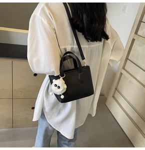 Close-up of black leather bucket bag with white sheep plush charm worn by model
