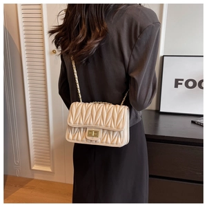 Detail of a beige pleated crossbody bag with gold chain strap shown on a model