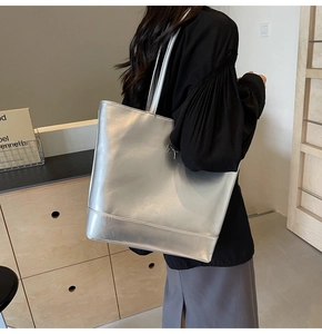 Detail of large silver PU leather tote bag with metallic finish shown on shoulder