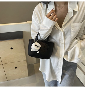 Close-up of black lychee leather mini bucket bag with a cute white fuzzy monster charm