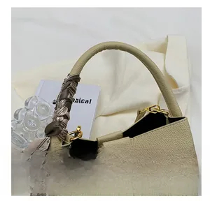 Detail view of beige leather bucket bag with silk scarf wrapped handle and gold hardware