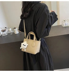 Model wearing a khaki lychee leather crossbody bucket bag with white plush charm