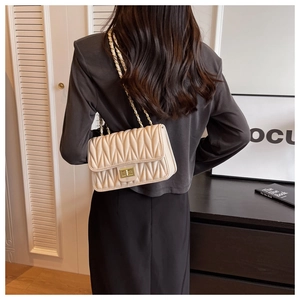 Detail of beige quilted crossbody bag with golden twist lock and chain strap on shoulder