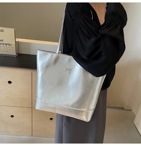 Close-up of a silver metallic PU tote bag with a delicate metal bow detail and long shoulder straps