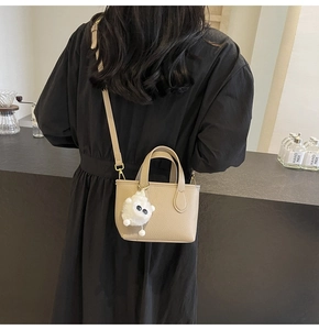 Back view of model carrying a beige lychee grain leather bucket bag with plush charm
