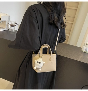 Chic beige lychee grain bucket bag with cute plush monster charm in a cafe setting