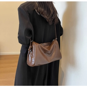 Detail view of brown leather shoulder bag with stylish knotted strap and pleated design