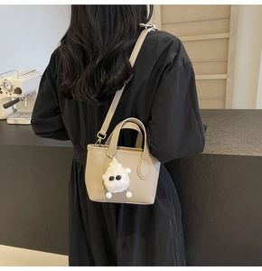 Detail of apricot pebbled leather bucket bag with cute plush charm on a black dress