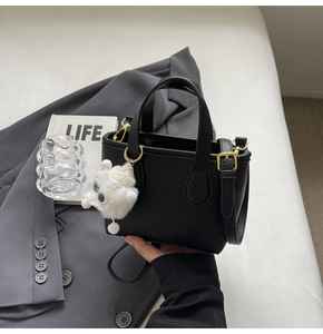 Detail of black pebbled leather bucket bag with gold hardware and white plush charm