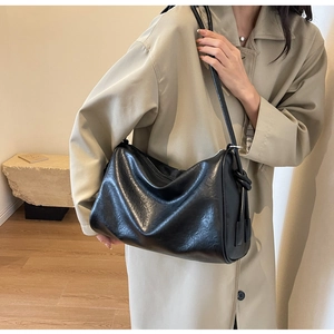 Detailed view of black soft leather Boston bag styled with a classic beige trench coat
