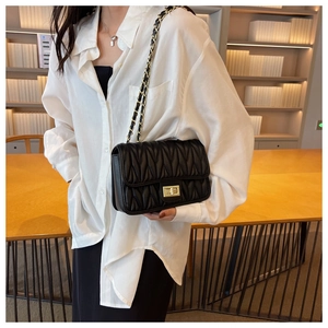 Close-up of black wave-quilted chain shoulder bag with gold twist lock and metal strap