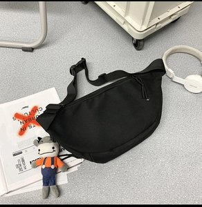 Top view of a black nylon crescent waist bag with adjustable strap and buckle on grey floor