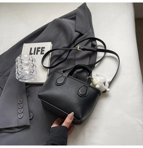 Detail of black lychee leather mini bucket bag with a cute white plush sheep charm