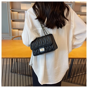 Detail of black matelassé crossbody bag with gold chain strap and turn-lock closure