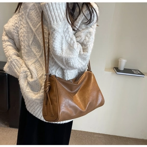 Close-up of brown PU leather Boston bag with decorative knot on white knit sweater