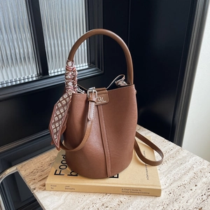 Detailansicht einer braunen Leder-Eimertasche mit kariertem Schal am Handgriff