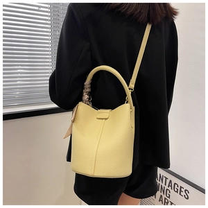 Detail of yellow bucket bag with lychee texture, silk scarf handle, and crossbody strap