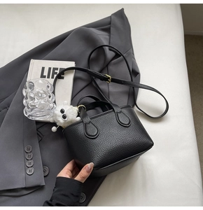Close-up of black litchi pattern mini bucket bag with a plush monster charm on a suit