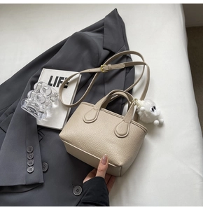 Detail of beige lychee texture leather mini bucket bag with a cute plush monster charm