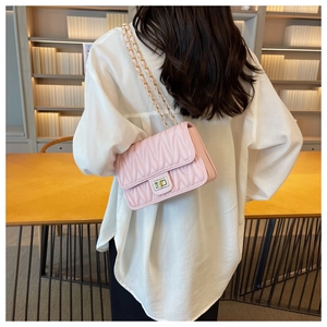 Close-up of pink quilted crossbody bag with gold metal chain strap on a female model