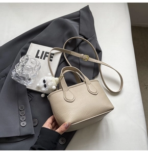 Detail of beige lychee grain leather tote bag with plush monster charm on a blazer
