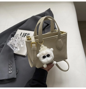 Detail of cream pebbled leather mini tote bag with plush monster charm and gold hardware