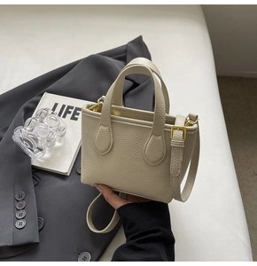 Detail view of cream bucket bag with lychee leather texture and golden metal hardware
