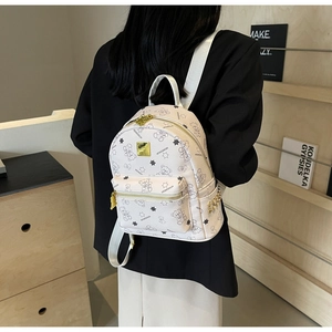 Detail eines weißen Lederrucksacks mit goldener Logo-Platte und Bärenmustern