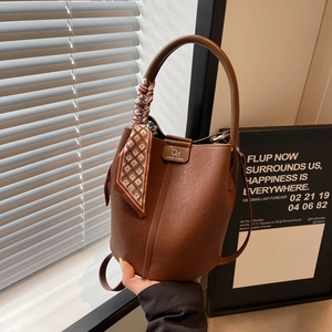 Detailansicht der braunen Leder-Eimertasche mit Metalllogo und rot kariertem Seidenschal