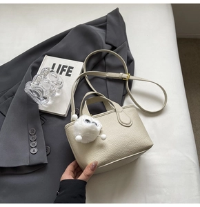 Close-up of beige lychee leather bucket bag with plush charm and gold hardware detail