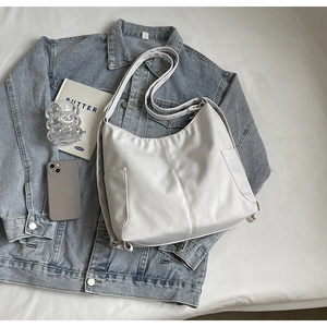 Detail van witte nylon draagtas met zijzakken gepresenteerd op denim jasje
