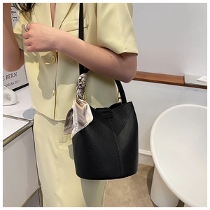 Detail of black textured leather bucket bag with elegant floral scarf handle on a model