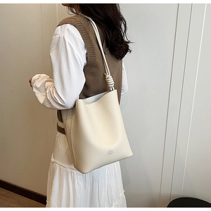 Detail view of beige lychee leather bucket bag showing knotted shoulder strap and texture