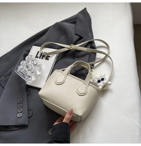 Detail of off-white lychee grain bucket bag with cute plush charm and adjustable strap