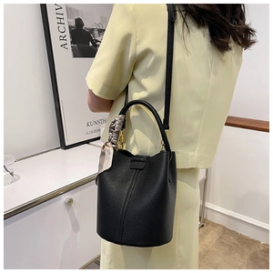 Detail of black pebbled leather bucket bag with decorative silk scarf on the handle