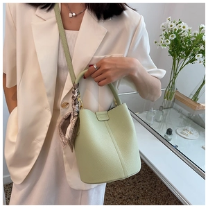 Close-up of light green bucket bag with lychee texture and decorative silk scarf handle