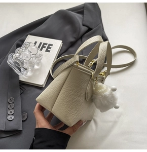 Close-up of beige lychee leather mini bucket bag with a white plush pompom charm